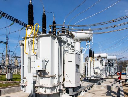 A huge industrial power transformer of a high-voltage substation at a power plant, against a background of blue sky.
